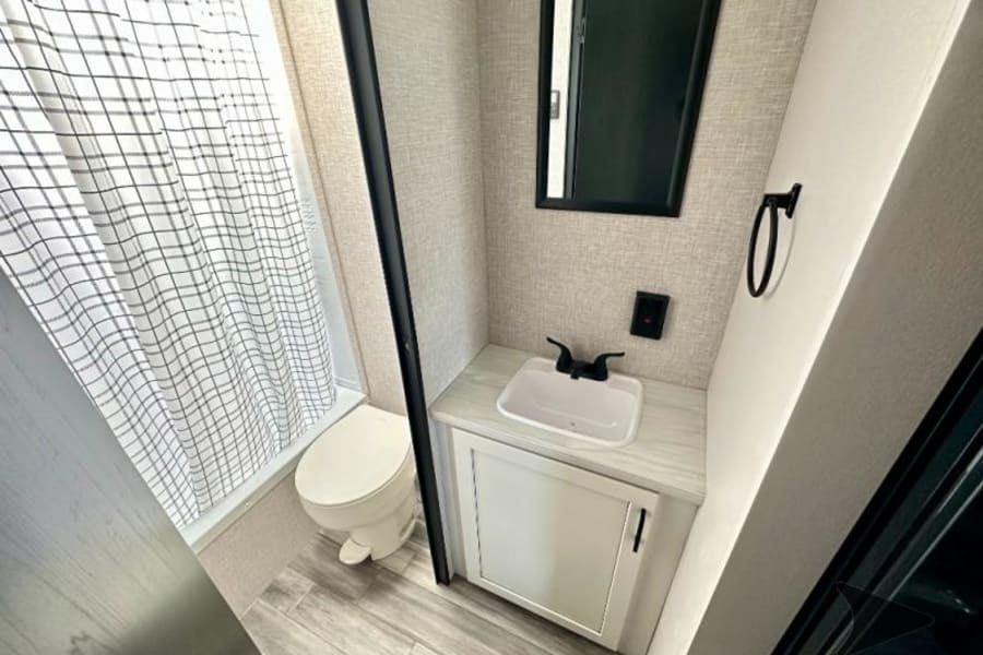 This RV rental features a compact, modern bathroom with a toilet, sink, mirror, and a plaid shower curtain.
