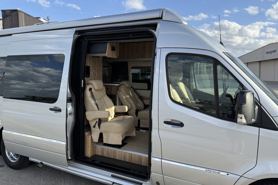 Luxury Airstream rv rental: Silver camper van, open side door reveals tan leather seats & wood interior. Ready for travel!