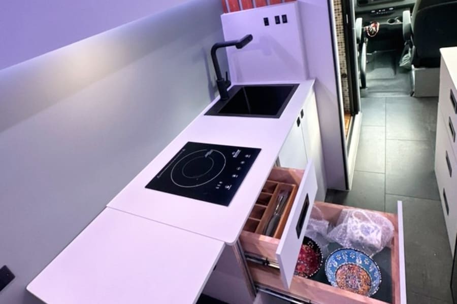 Compact RV rental kitchen with sink, induction cooktop, extendable counter, and pull-out drawers for storage.