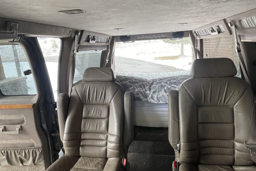 Step inside this RV rental: plush leather seating & a rear bed in a customized conversion van interior.