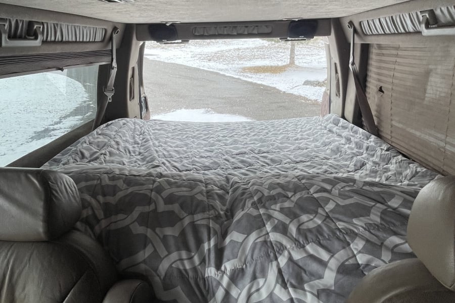 Cozy RV rental interior with a comfortable bed and a winter road view from the back.
