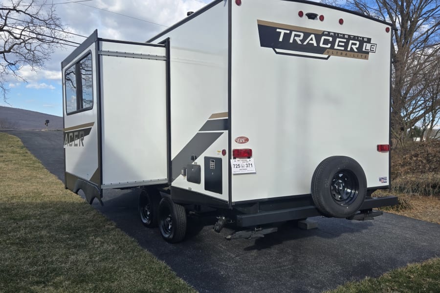 White Tracer LE travel trailer, an rv rental, parked on an asphalt lot with its slide-out extended for outdoor living.