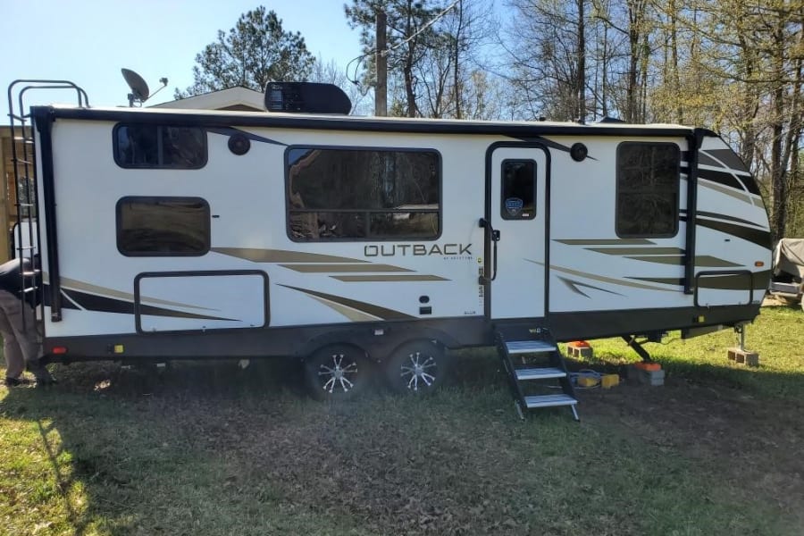 White Outback travel trailer RV rental parked on grass, ready for adventure with steps & roof antenna.