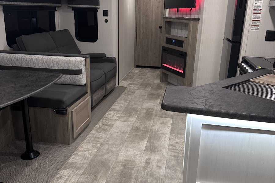 Modern RV rental interior with dinette, kitchen, fireplace, and ambient red lighting, showcasing the living space.