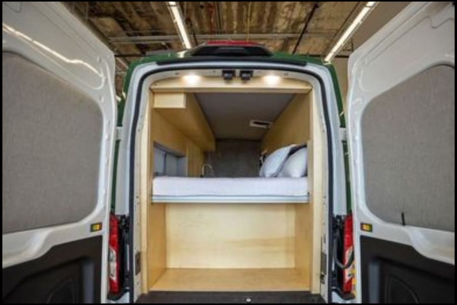 This RV rental shows a cozy camper van interior with a bed and under-bed storage, perfect for your next adventure.