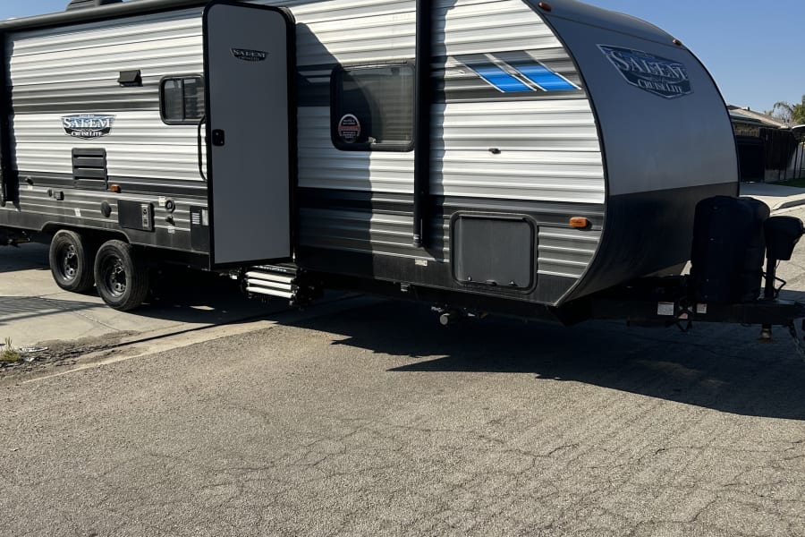 Grey Salem Cruise Lite travel trailer (RV rental) parked on asphalt under a clear sky. Door open, steps out.