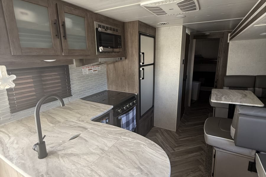 Spacious rv rental interior showing kitchen with stove, fridge, and dinette. Modern design for comfortable travel.