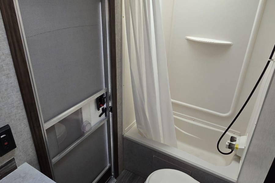 Experience comfort in this RV rental bathroom, featuring a compact toilet, shower/tub, and vanity sink. Perfect for your travels.