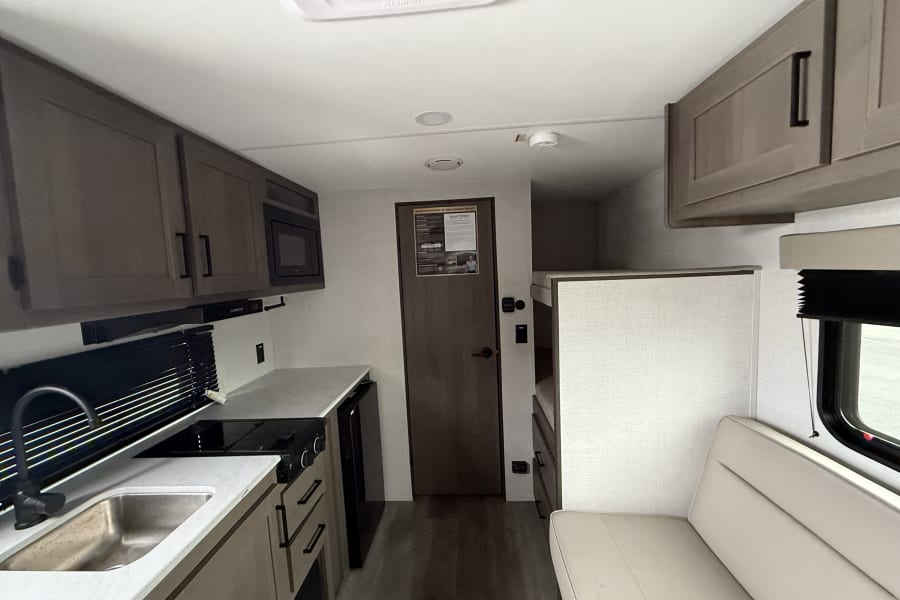 Interior of a modern RV rental, showcasing a compact kitchen, comfortable seating area, and built-in bunk beds.