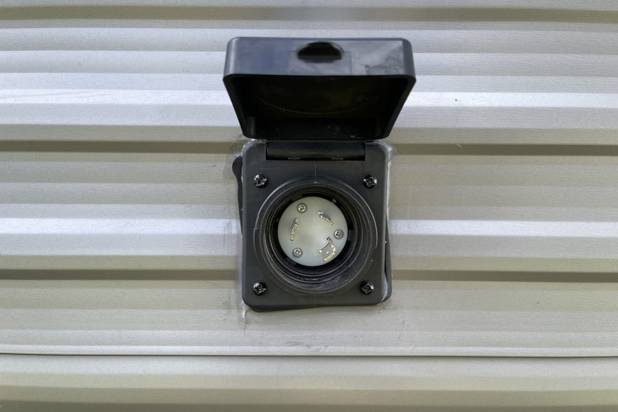 Close-up of an RV rental's 30-amp electrical power inlet on its side, cover open, showing the female receptacle.