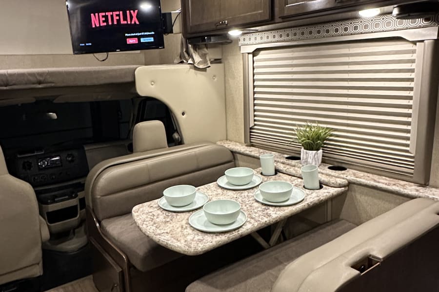 Cozy RV rental interior featuring a dining area, overhead Netflix TV, and a front bunk bed, ready for your next trip.