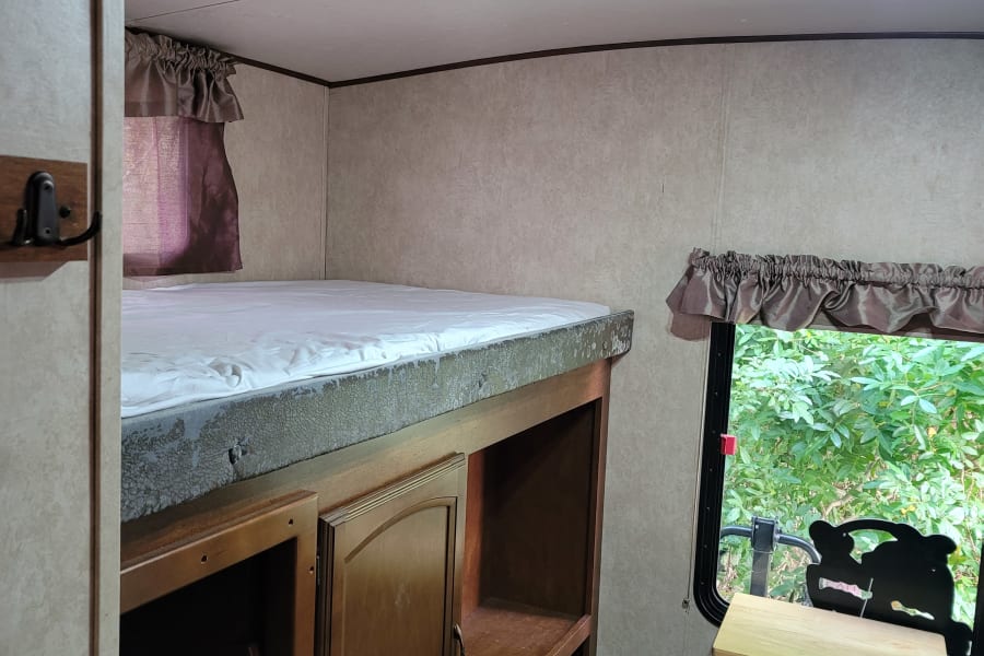 RV rental interior featuring a bunk bed with a white mattress, wooden storage unit, ladder, and a window with green outdoor view.