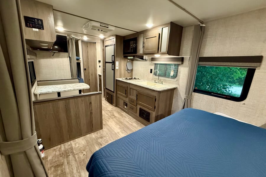 Inside a modern **rv rental**, featuring a full kitchen, comfortable bed, and dinette area, showing a functional layout.