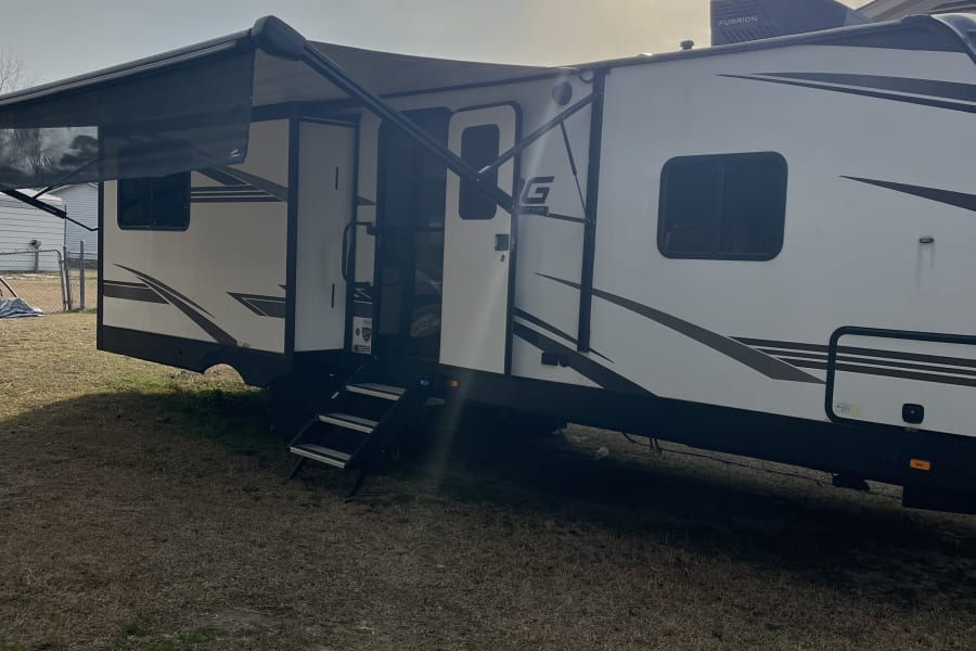 Bright RV rental: A white travel trailer with an extended awning and entry steps, parked outdoors on a sunny day.