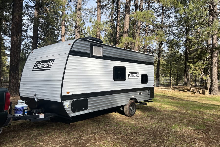 Coleman travel trailer parked amidst pine trees, ideal for an RV rental or camping getaway in nature.