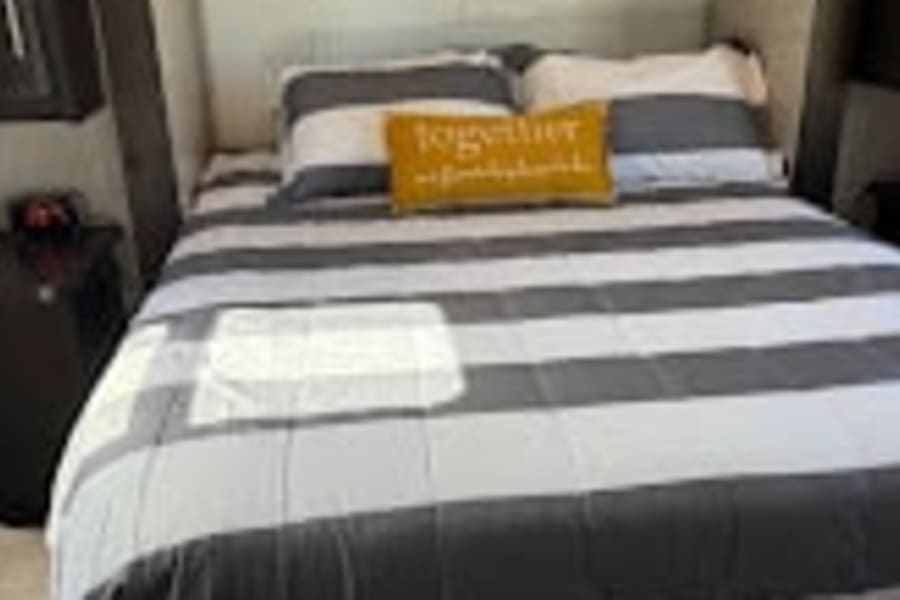 Comfortable RV rental bedroom setup with grey & white striped bedding, perfect for your next travel accommodation.