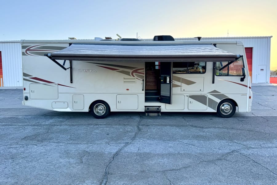 White Vista RV rental with awning extended, door open, parked on cracked asphalt. Ideal for your next motorhome travel adventure.