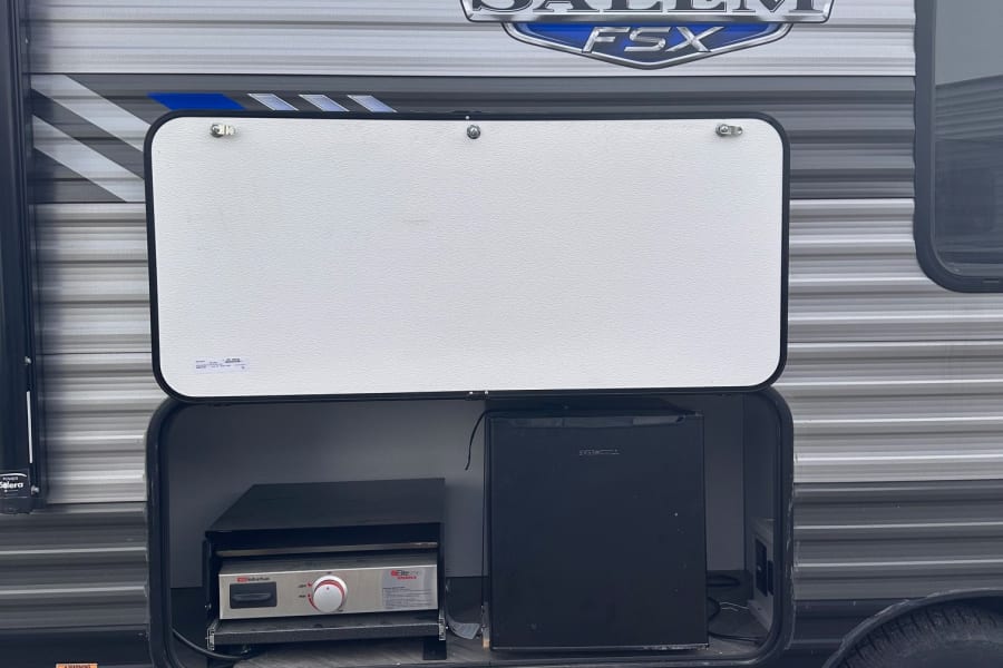 Explore this RV rental's convenient outdoor kitchen featuring a griddle and mini-fridge for easy meals on the go.
