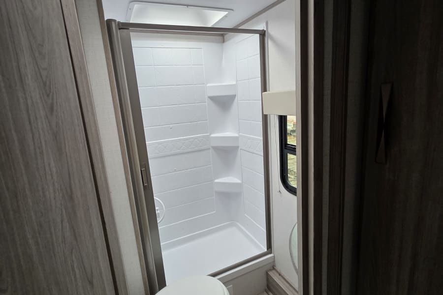 Inside an RV rental: a bright, compact bathroom featuring a shower, toilet, and ceiling fan for ventilation.