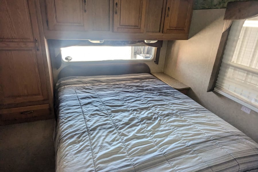 RV rental bedroom with a cozy striped bed, ample overhead wooden cabinets, and a bright window.