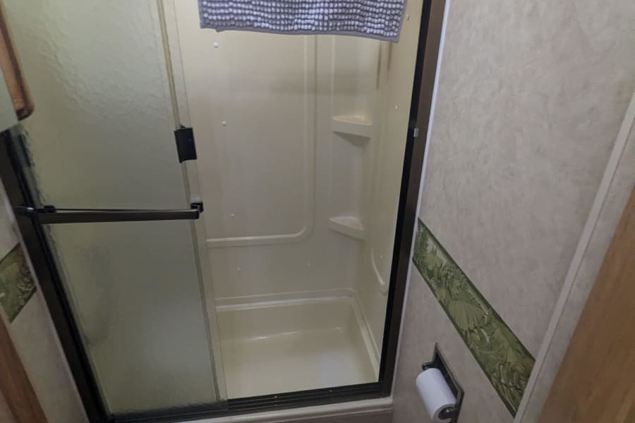 RV rental bathroom with a compact stand-up shower, toilet, and light-colored walls. A practical space for your travels.