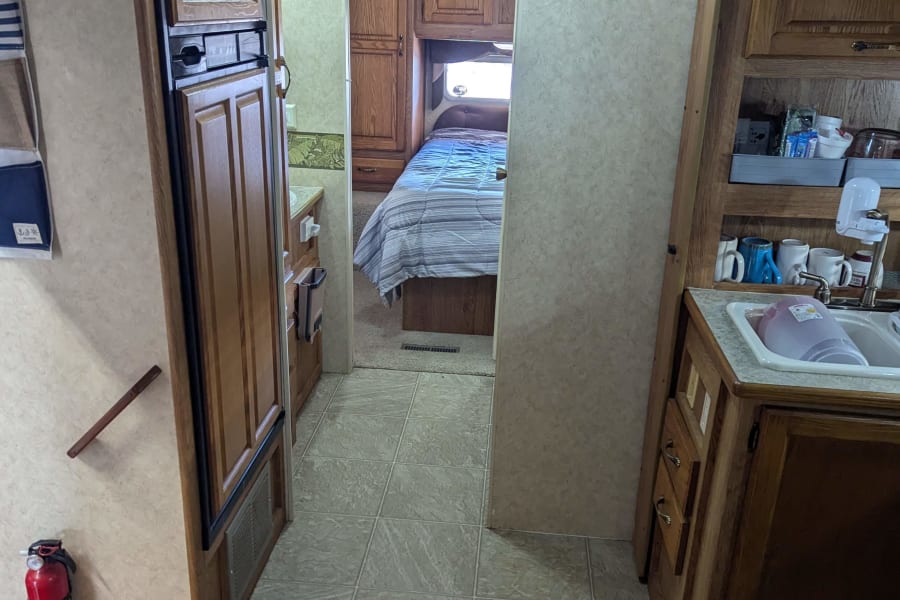 RV rental interior featuring a practical kitchen, tiled hallway, and cozy bedroom with wood cabinetry. Fire extinguisher visible.