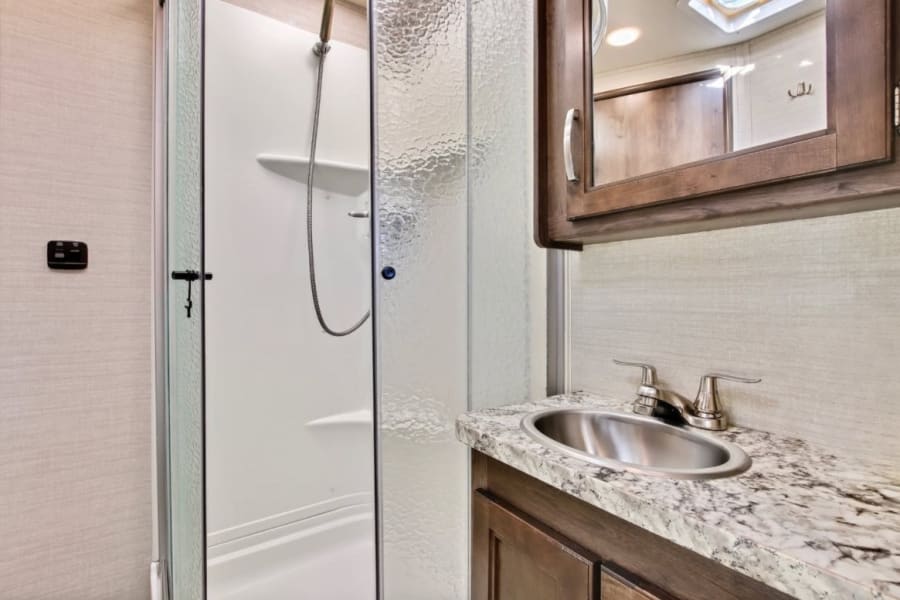 An RV rental bathroom with a compact shower, vanity sink, and mirrored medicine cabinet.