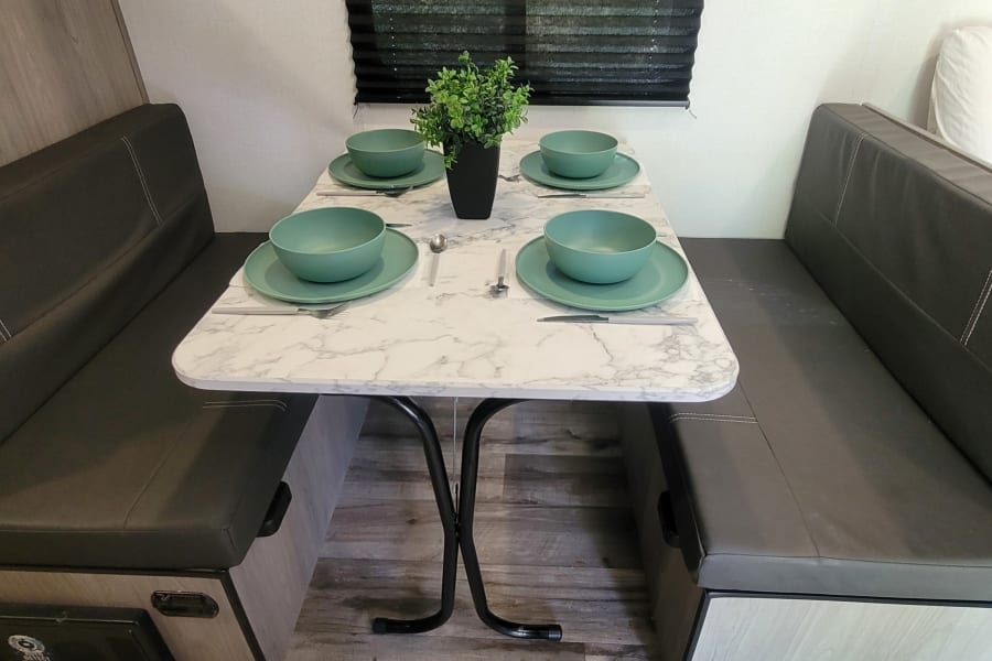 This RV rental features a compact dinette with a marble-patterned table, set for four with green dishes, flanked by cozy gray benches.