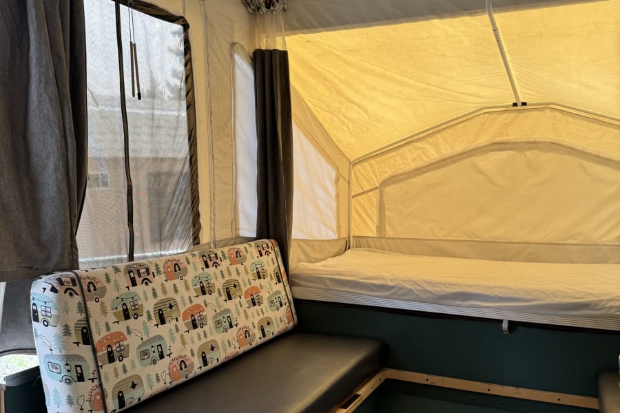 Interior of a comfortable pop-up RV rental, featuring a bench, bed, and essentials for your next camping adventure.