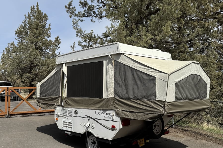 Pop-up RV rental: A Rockwood Freedom camper extended on asphalt with power cord, ready for your camping travel.