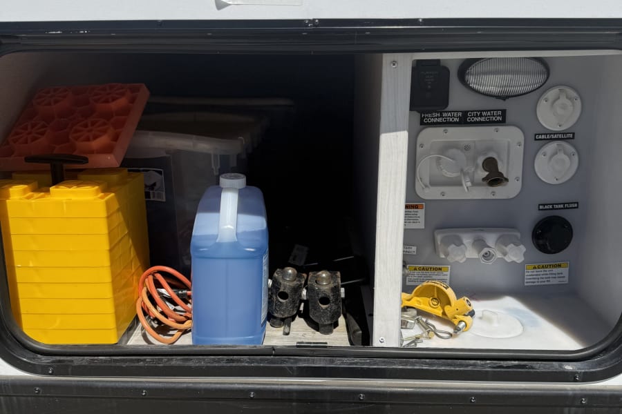 RV rental's exterior utility panel for water, cable, and solar, plus stored leveling blocks & winterizing fluid.