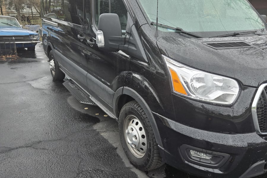 Black high-roof van, suitable for RV rental, parked on wet pavement with side steps and rain droplets.