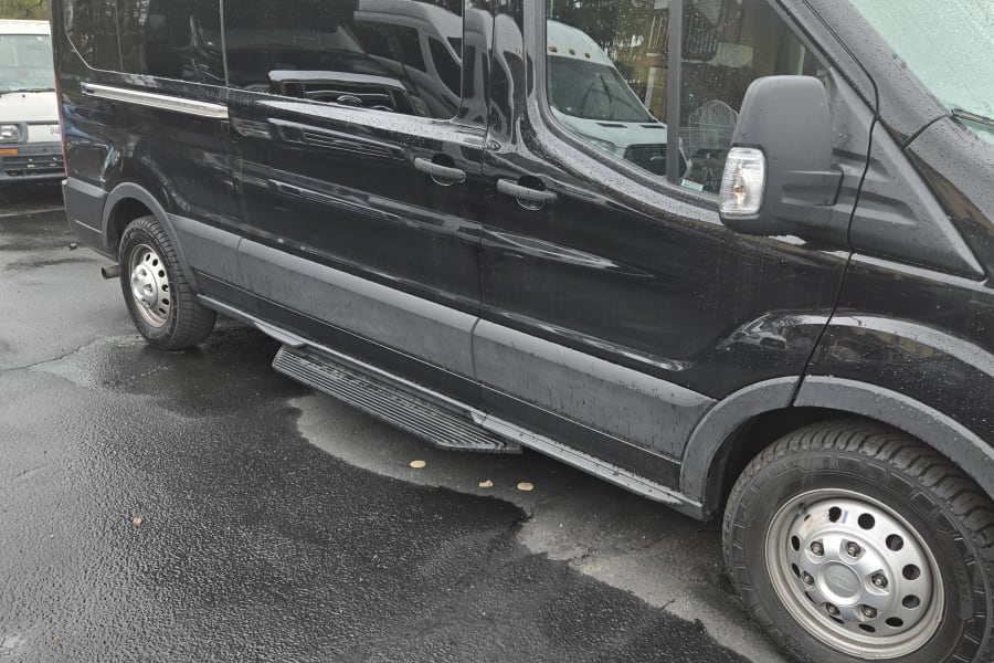 This black passenger van, a versatile RV rental option, is shown parked on wet pavement after rain.