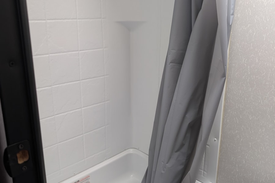 This RV rental features a compact white shower/tub combo with a gray curtain and a partial view of the toilet.