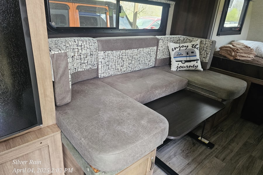 Cozy RV rental interior featuring a U-shaped dinette, large windows, and a bed area, perfect for travel.
