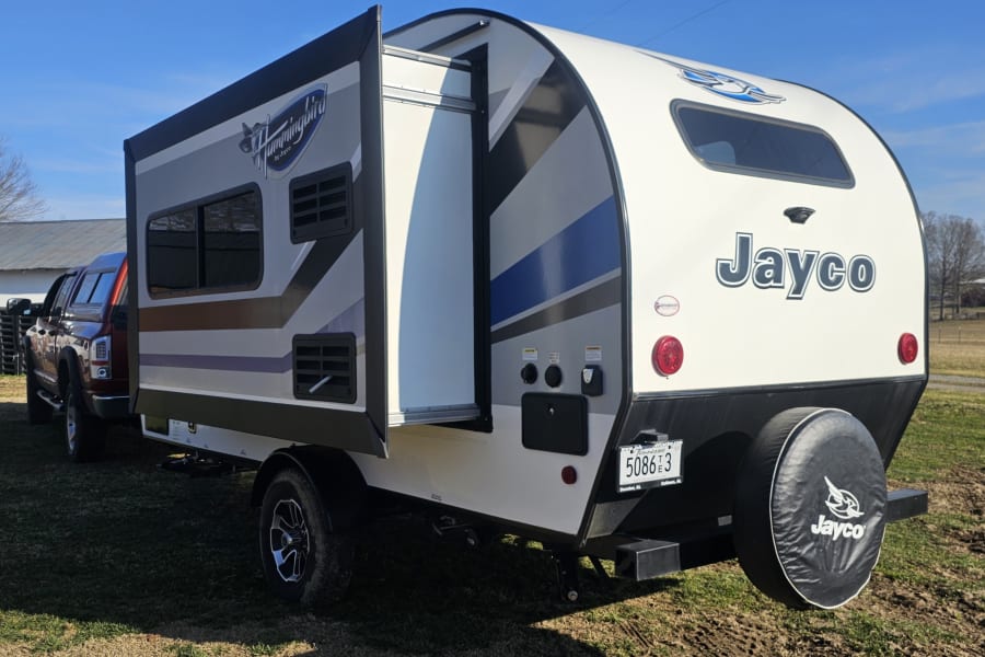 A white Jayco Hummingbird travel trailer with a slide-out extended, parked outdoors. This spacious RV is ideal for your next rv rental.