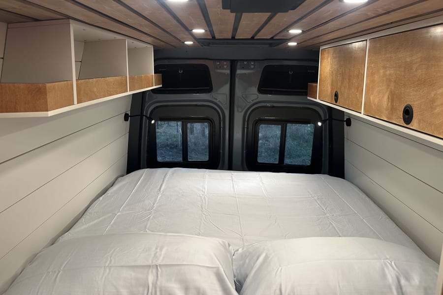 Cozy RV rental interior featuring a comfortable bed, built-in storage, stylish ceiling, and scenic rear windows.