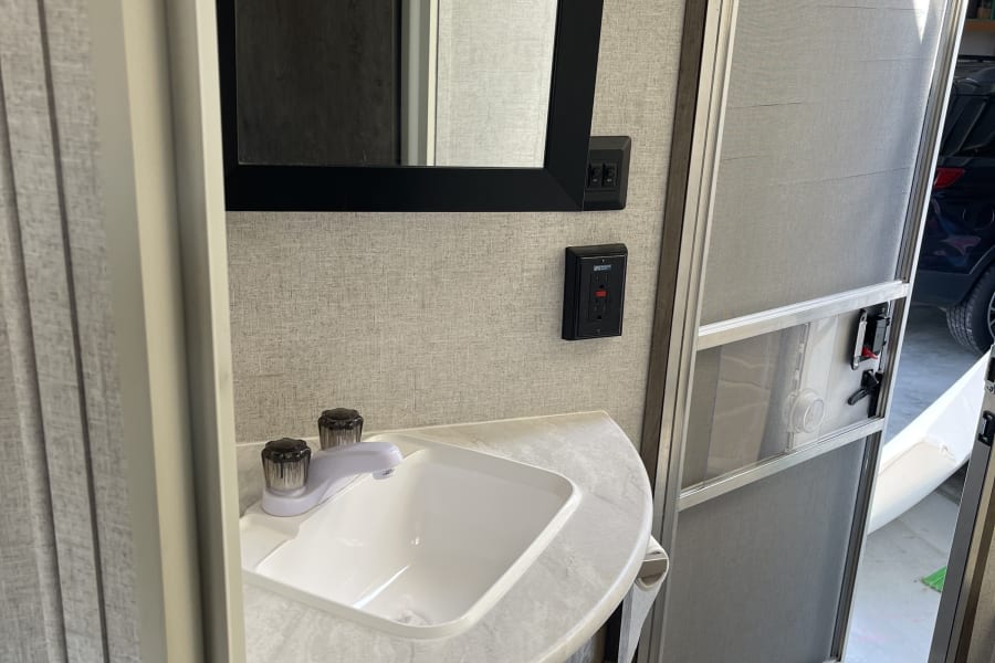 RV rental: Inside, a compact bathroom sink, mirror, and the RV's screen door open to the outside.