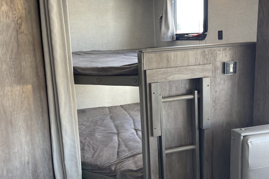 Inside an RV rental: two cozy bunk beds with a ladder and privacy curtain, ideal for family adventures.