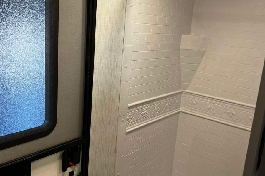 Inside an RV rental: a compact bathroom featuring a subway-tile-style shower, modern sink, and adjacent entry door.