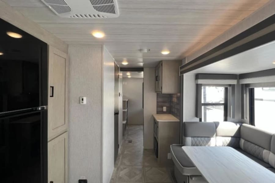 Modern RV rental interior with spacious living/dining area, compact kitchen, and hallway leading back.