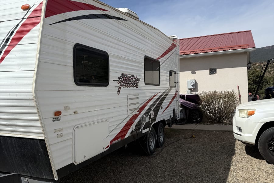 White Altitude travel trailer RV rental parked on gravel near a house and white SUV, ready for adventure under blue skies.