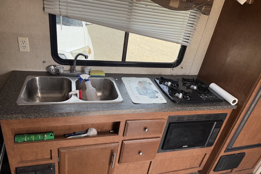 Inside an RV rental: a compact kitchen featuring a dual sink, 3-burner stove, and Sunbeam microwave.
