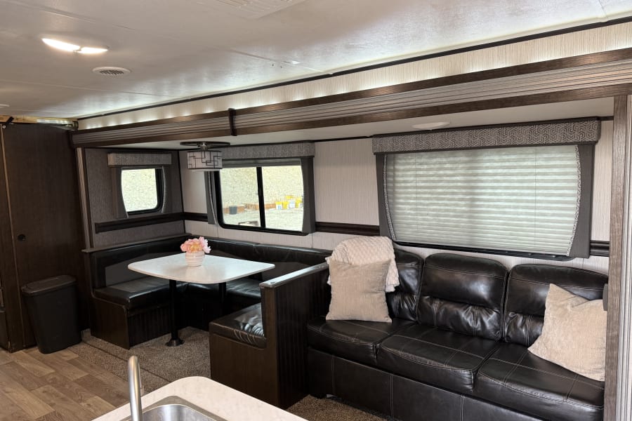 Spacious RV rental interior with a cozy dinette, black leather sofa, and kitchen area, showcasing comfortable living space.
