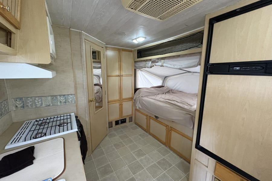 Inside an RV rental: a compact kitchen with a stove, a cozy bed area, and ample built-in storage.