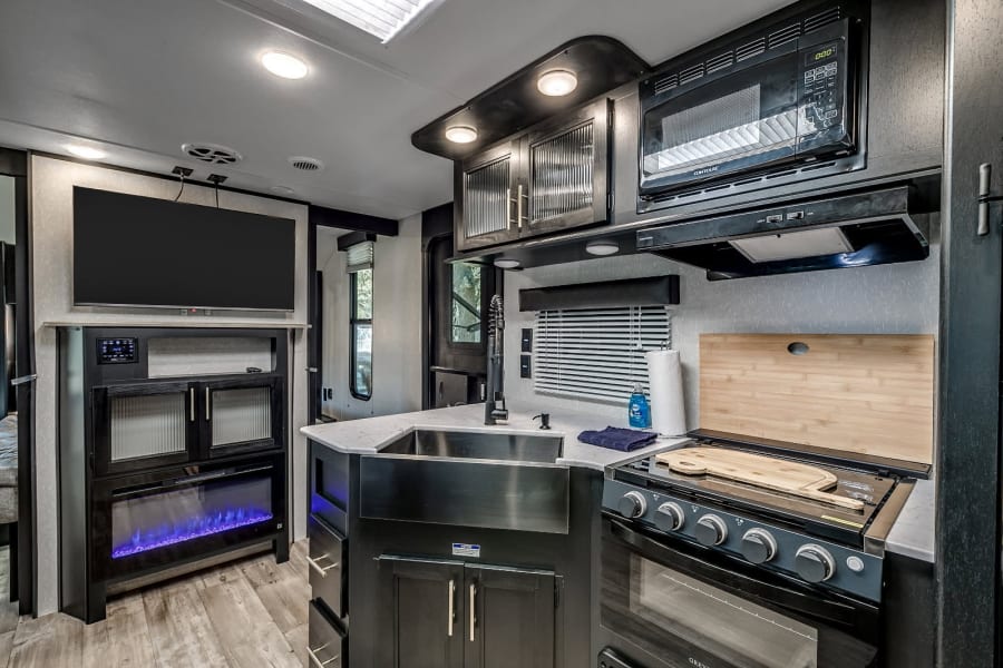 RV rental: Spacious interior with modern kitchen (sink, stove, microwave), entertainment center, and electric fireplace.