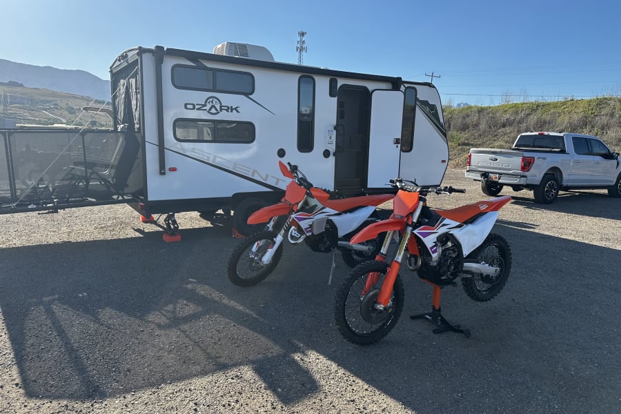 Ozark Ascent RV rental, two KTM dirt bikes, and a Ford F-150 truck parked for an outdoor adventure.