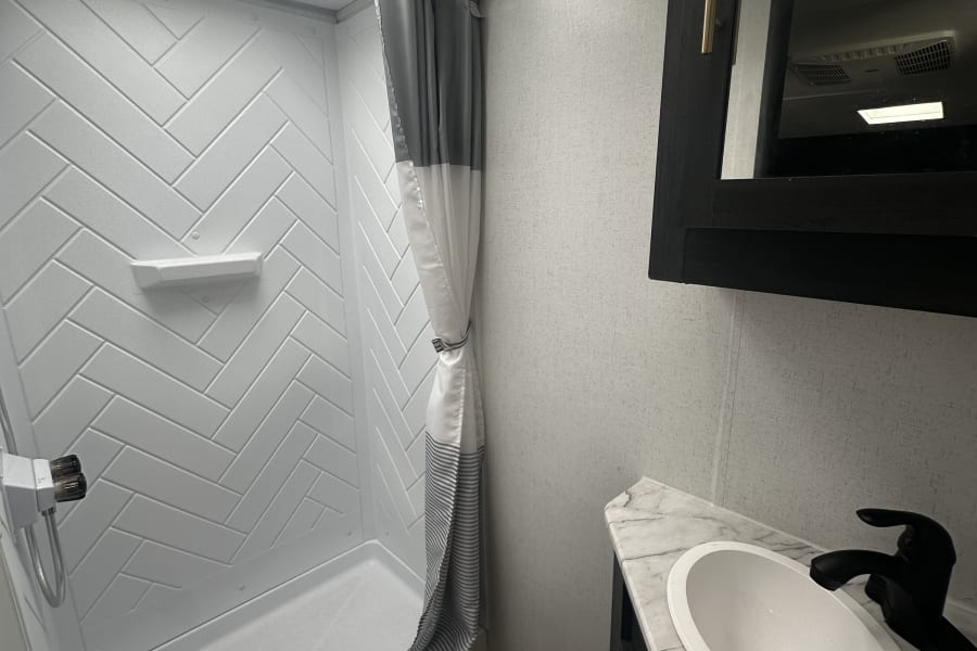 Clean RV rental bathroom: herringbone shower, toilet, and modern vanity with sink and marble-look counter.