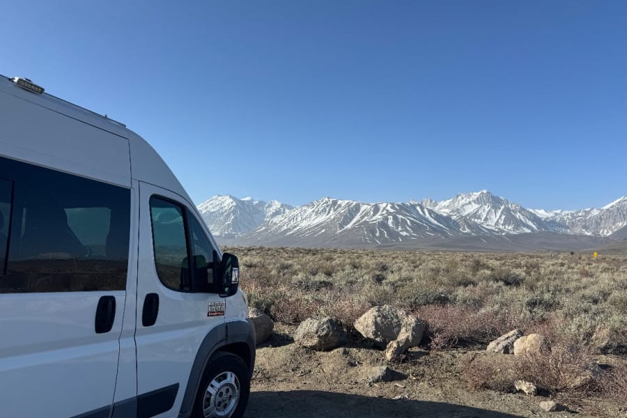 Scenic morning wake-up from an RV rental! White camper van faces majestic snow-capped mountains in desert.