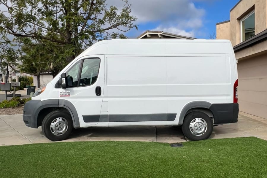 White cargo van, often used for rv rental or deliveries, parked on a driveway next to artificial grass.